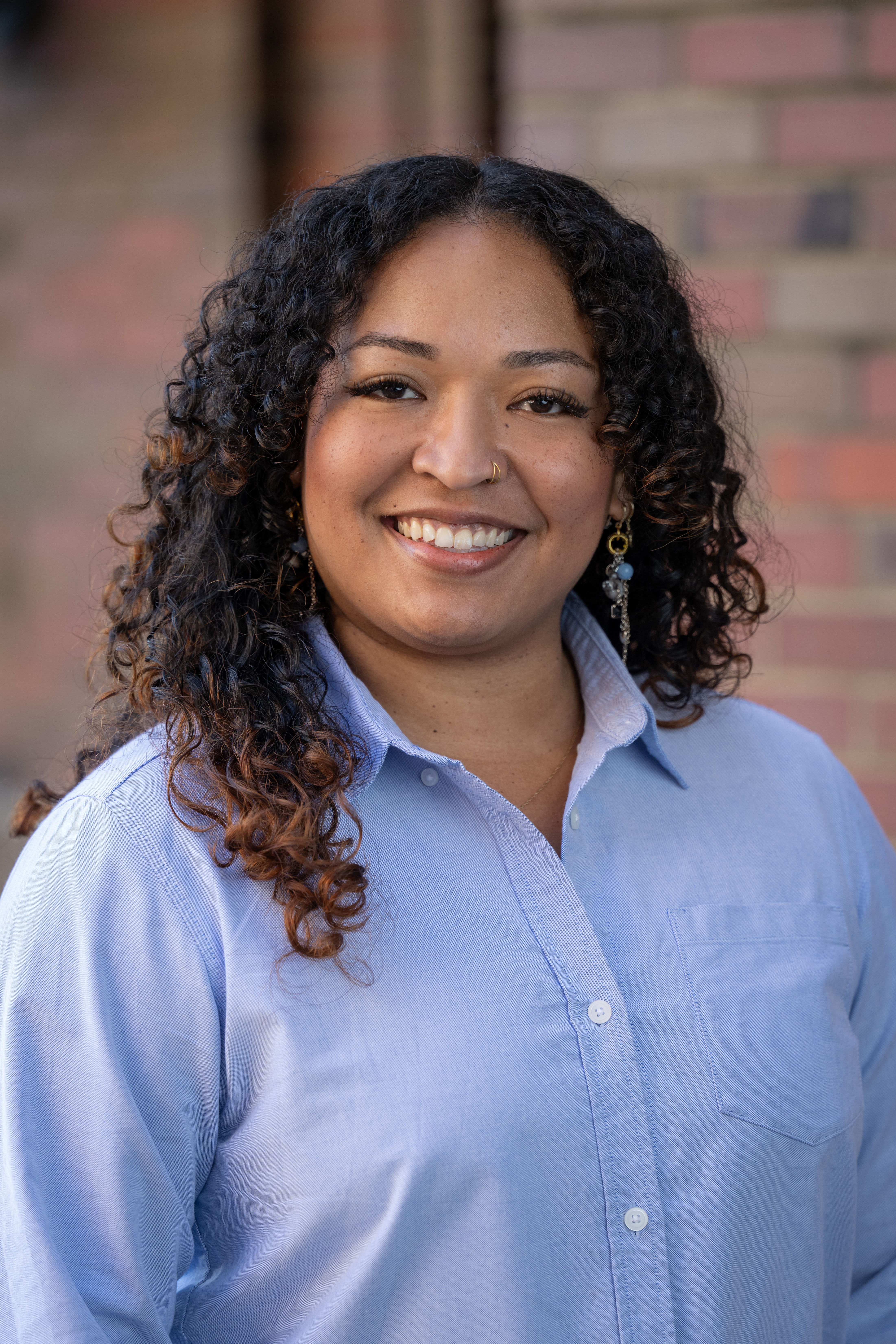 Portrait of Jasmine Banks, smiling, standing in front of a brick wall.